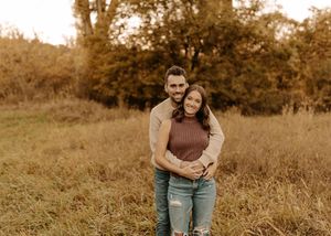 Couple embracing in an autumn field, surrounded by golden trees and tall grass, in a warm fall outdoor photo session.
