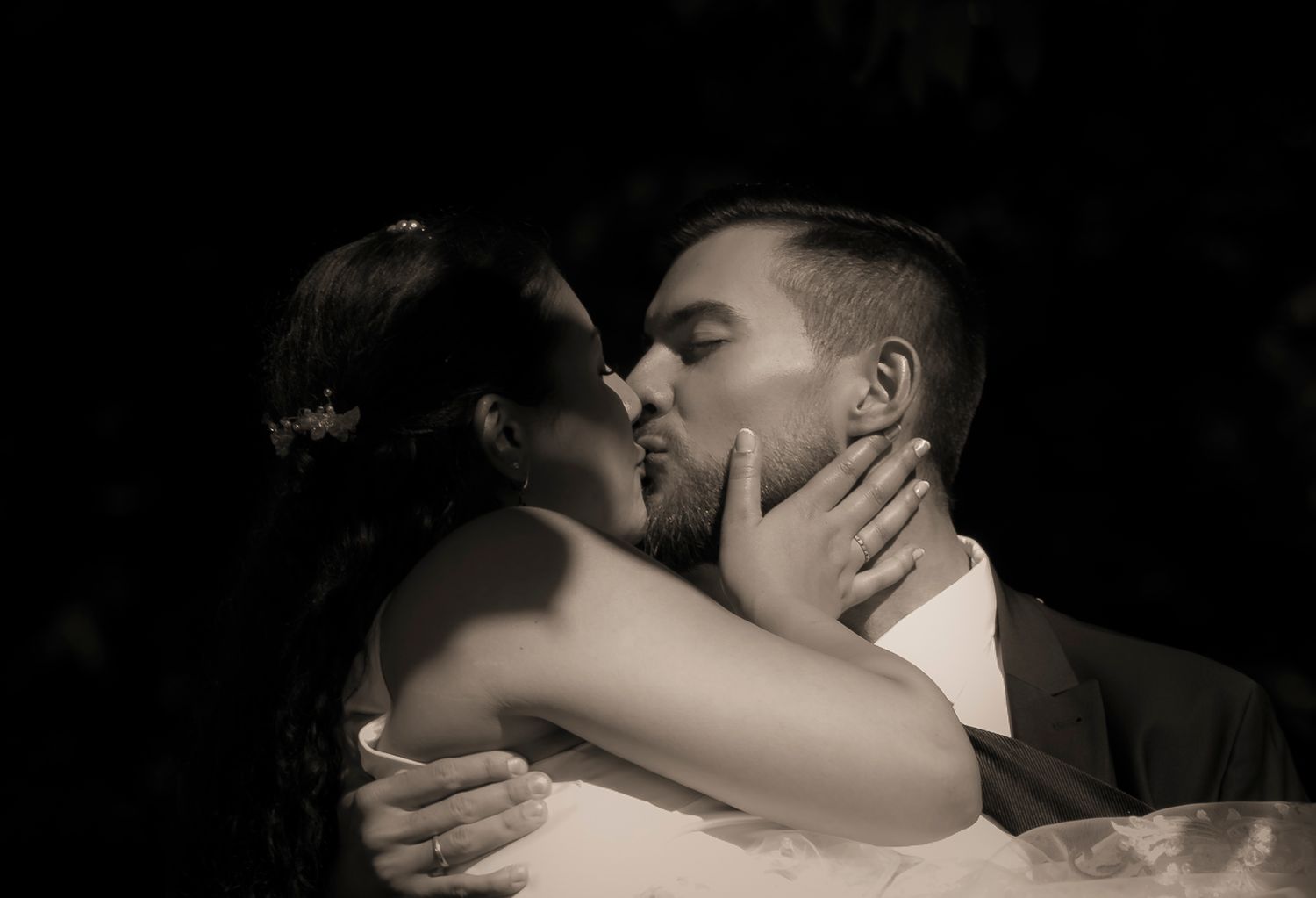 Romantic black and white photo of newlyweds sharing first kiss in dramatic lighting.
