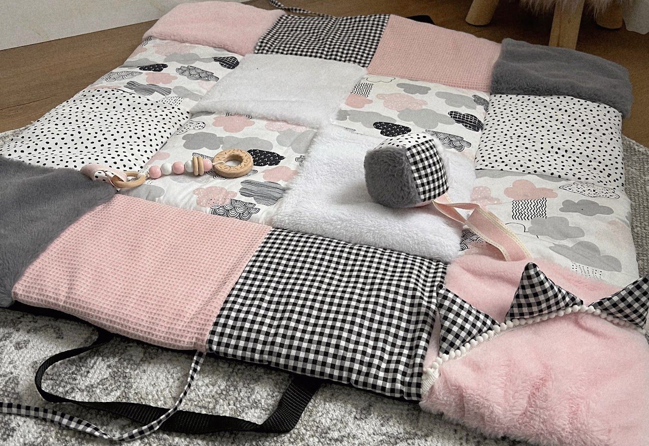 Pink, gray, and white patchwork baby play mat with toys, featuring gingham, cloud prints, and soft textures.