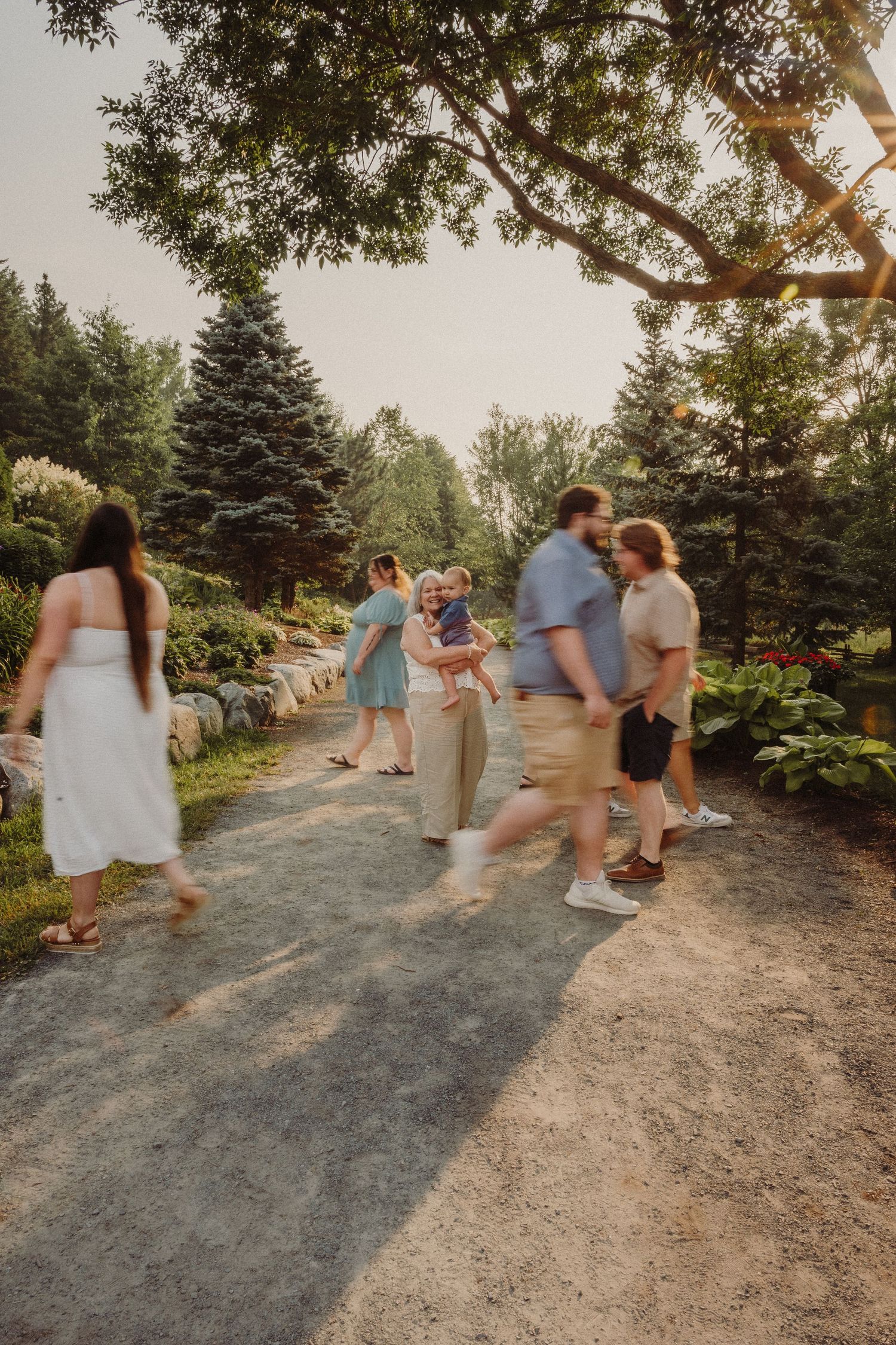 Expectant mother poses in sage green dress among blooming cherry trees at sunset.