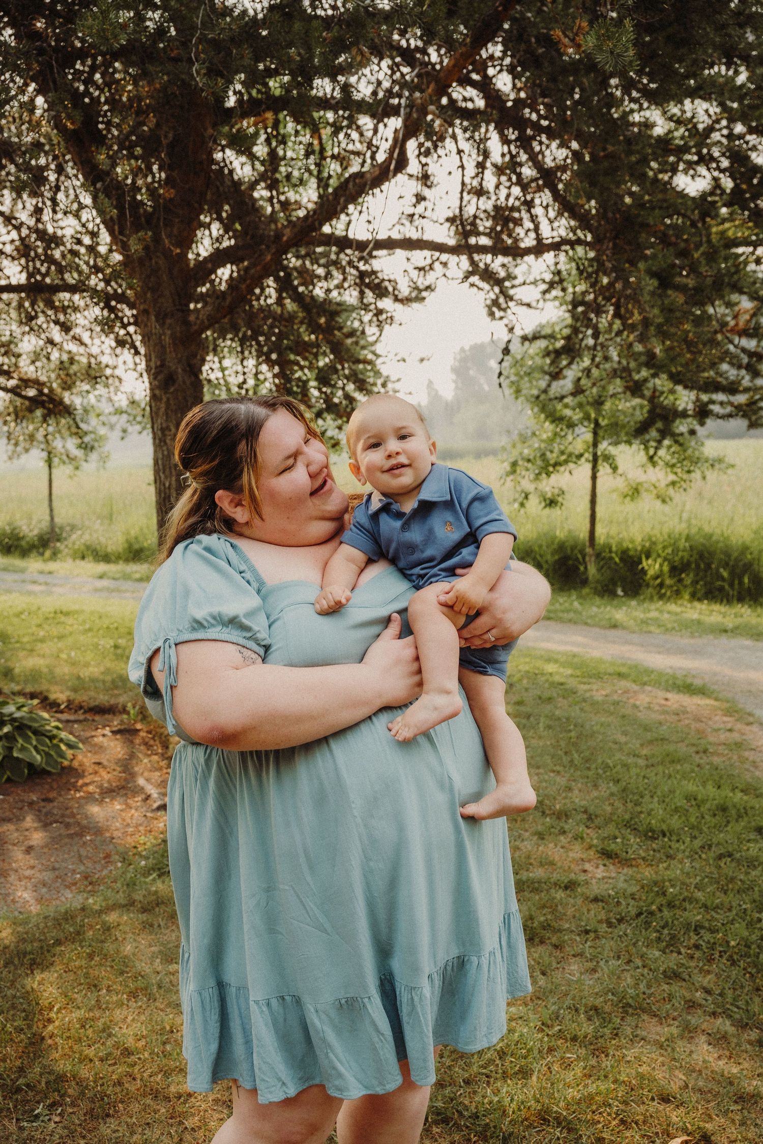 Expecting mother in a blue dress poses on a sunlit nature path.