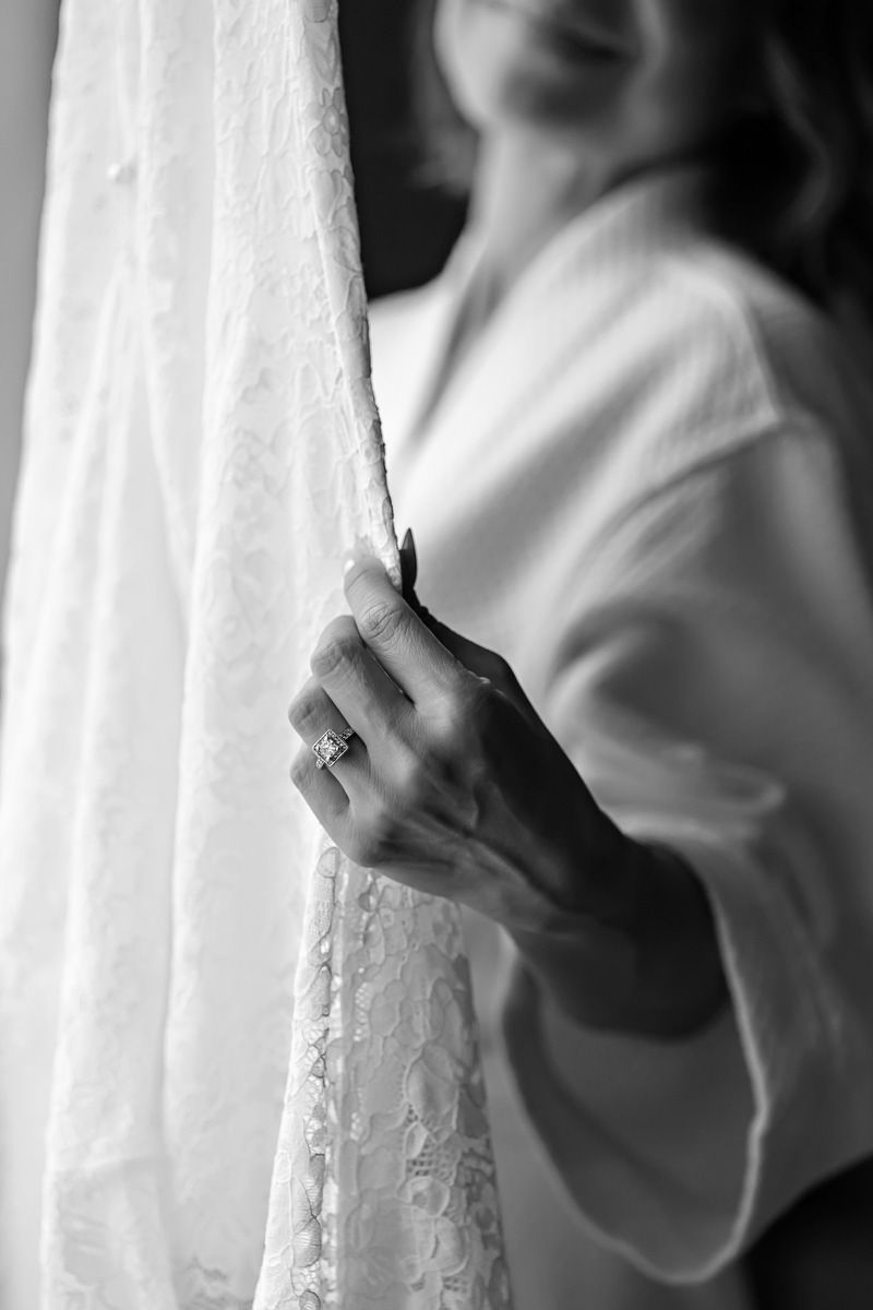 Black and white photo of a bride holding her lace wedding dress, showcasing her diamond engagement ring.