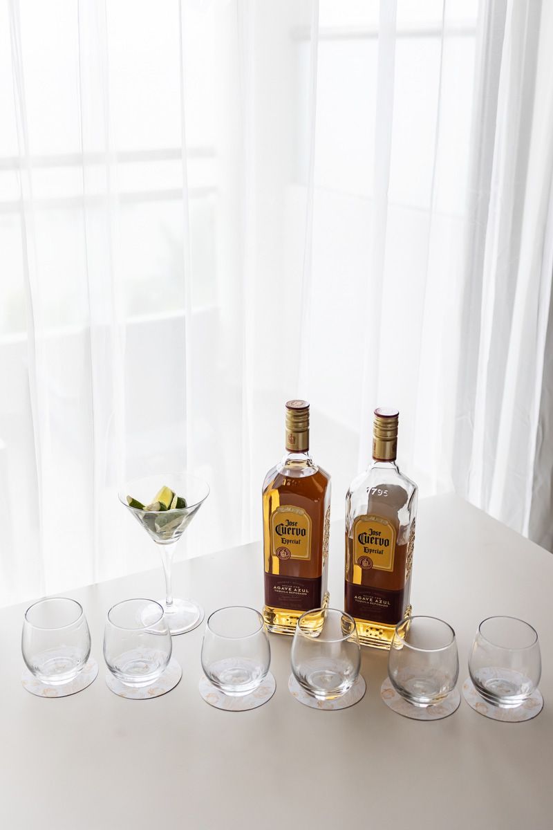 Two Jose Cuervo tequila bottles with empty stemless glasses and a martini glass with lime on a white table.