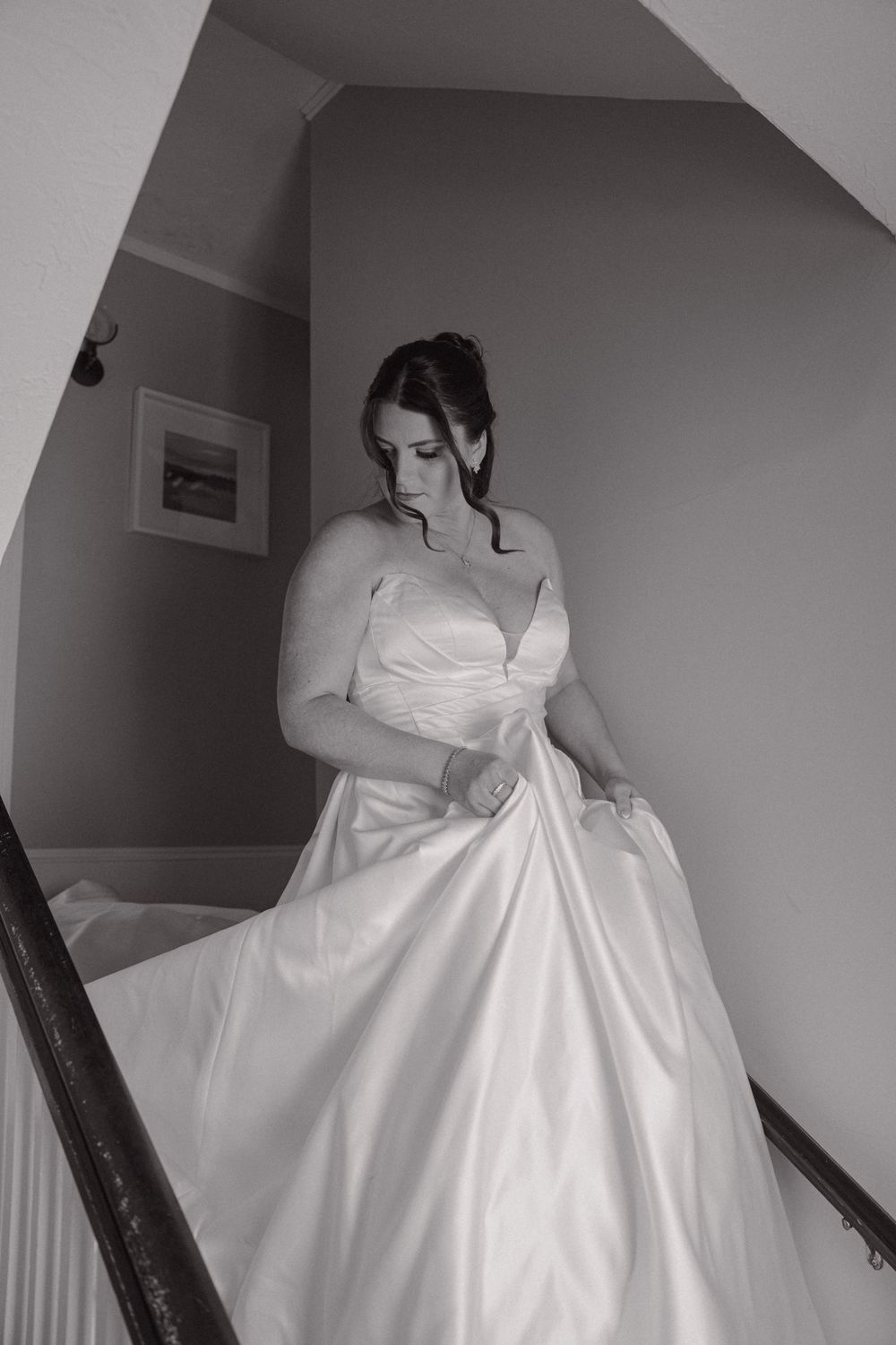 Bride in a strapless satin ball gown descending stairs in a black and white wedding photo.