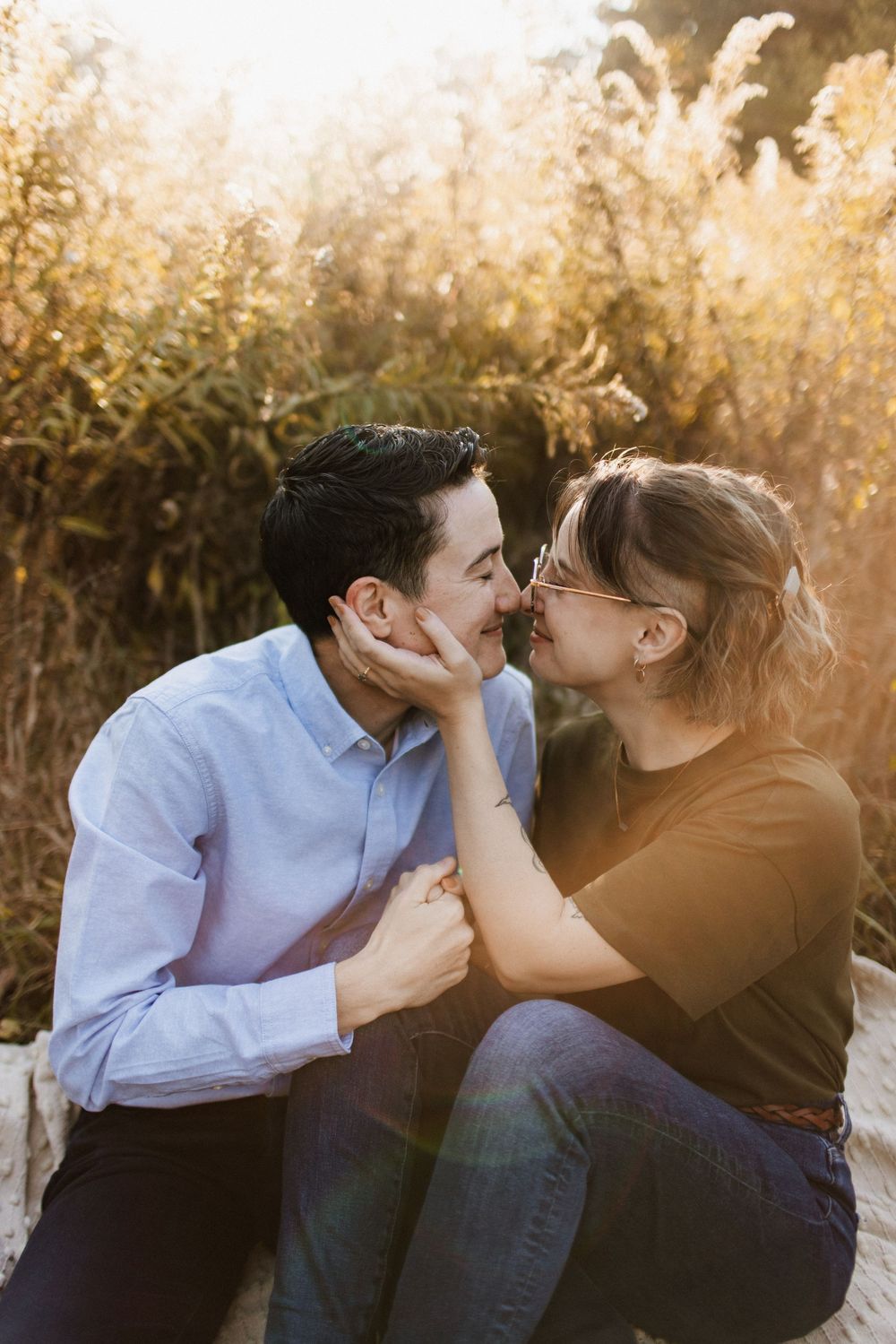 Couple sharing a romantic almost-kiss outdoors in golden sunlight, surrounded by tall autumn grasses.