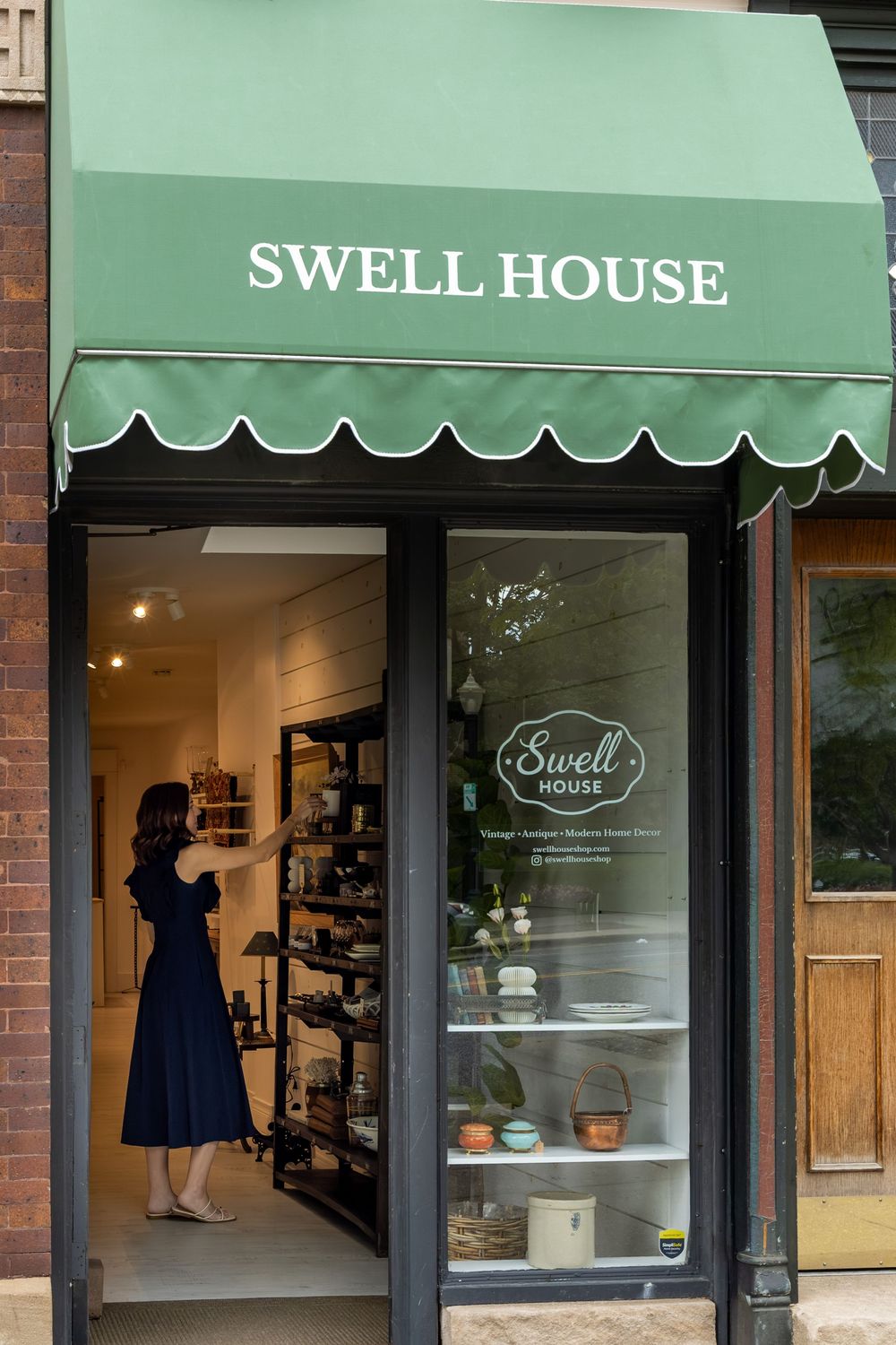 Swell House La Grange boutique storefront with green scalloped awning, glass door, and woman browsing shelves inside.