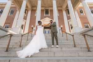 Bride and groom pose on grand staircase of elegant brick building with white columns during outdoor wedding ceremony.