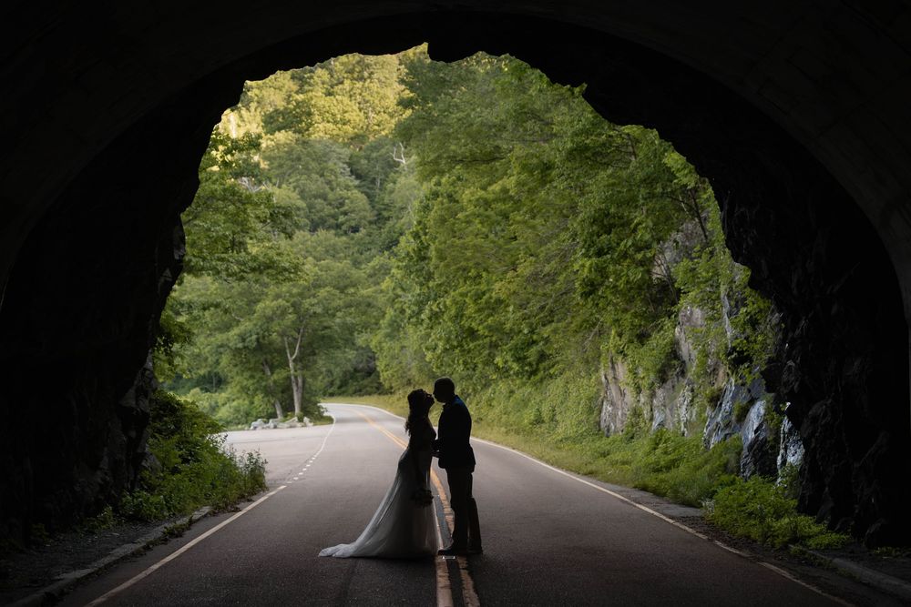 Silhouette of a wedding couple kissing inside a tunnel framed by lush green trees and rocky cliffs.
