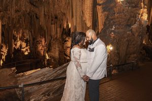 Couple holds hands in a stunning cave wedding ceremony surrounded by glowing stalactites and stalagmites.