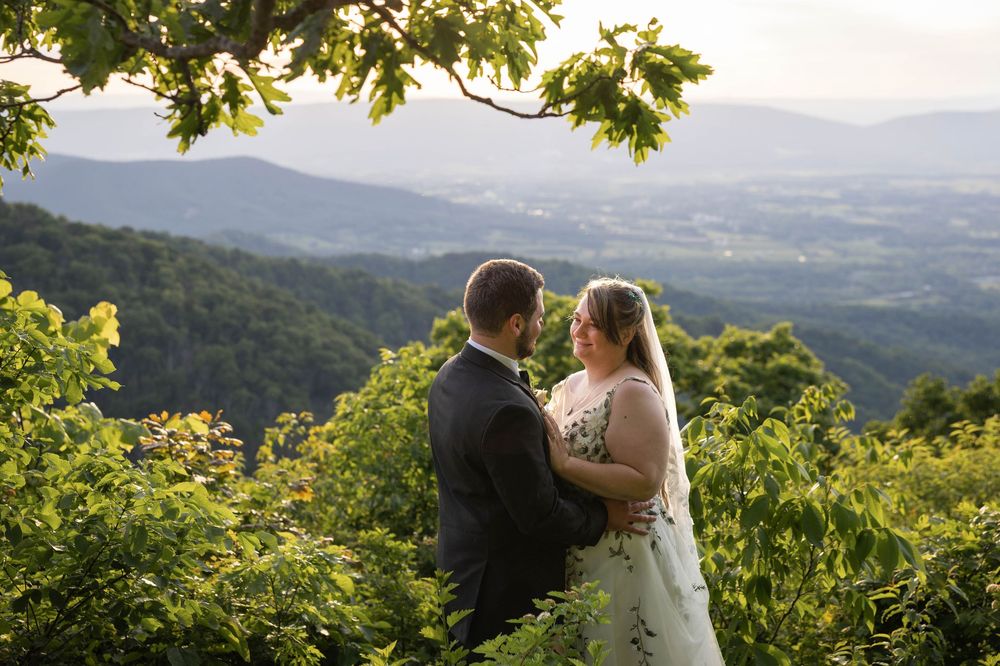 Bride and groom share a romantic moment on a mountain overlook surrounded by lush green trees and rolling Virginia hills.