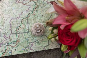 Wedding rings in velvet box on map with pink lily and red rose bouquet for romantic travel-themed wedding.