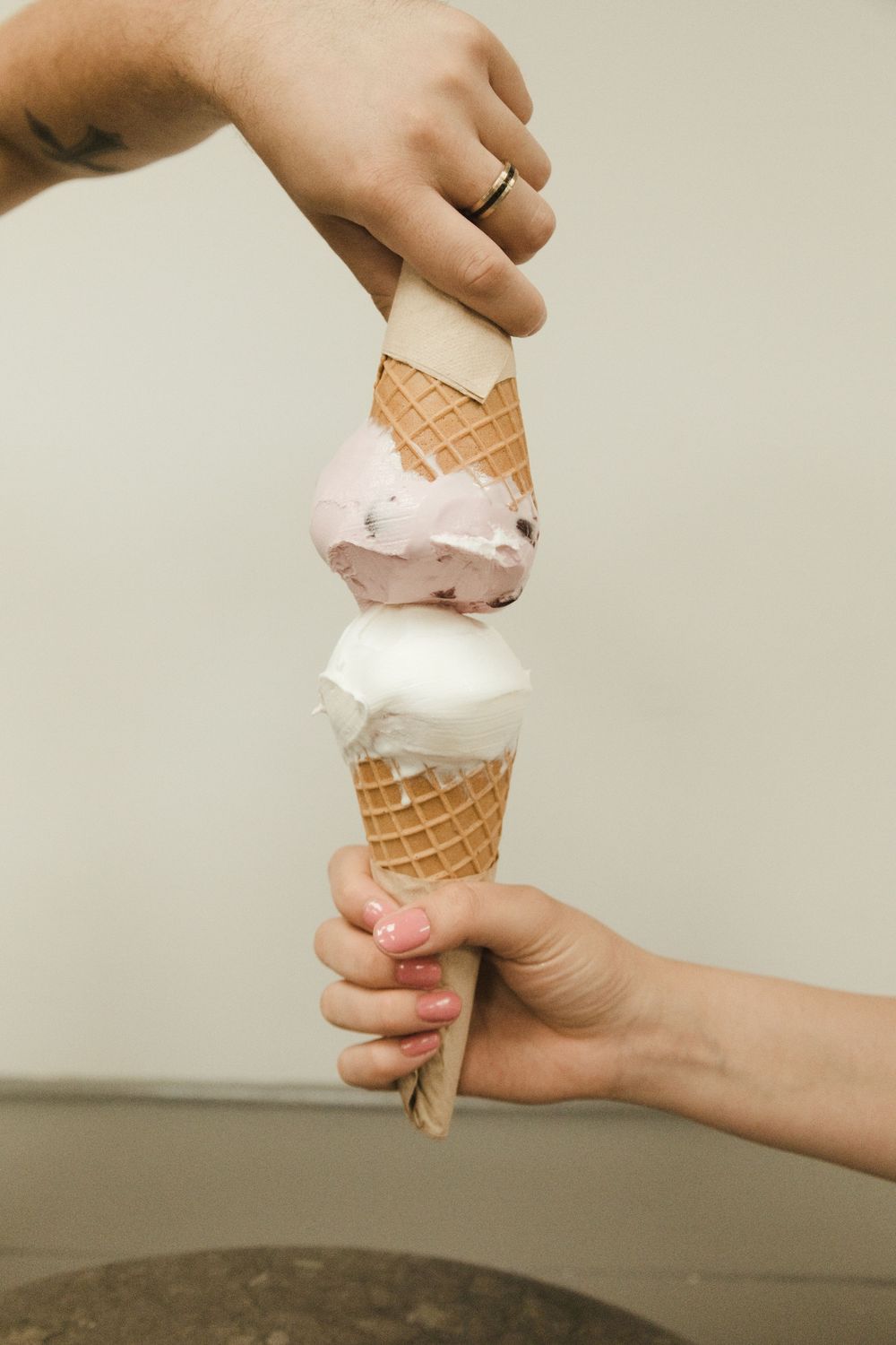 Two hands holding a double scoop ice cream waffle cone with white and purple flavors.