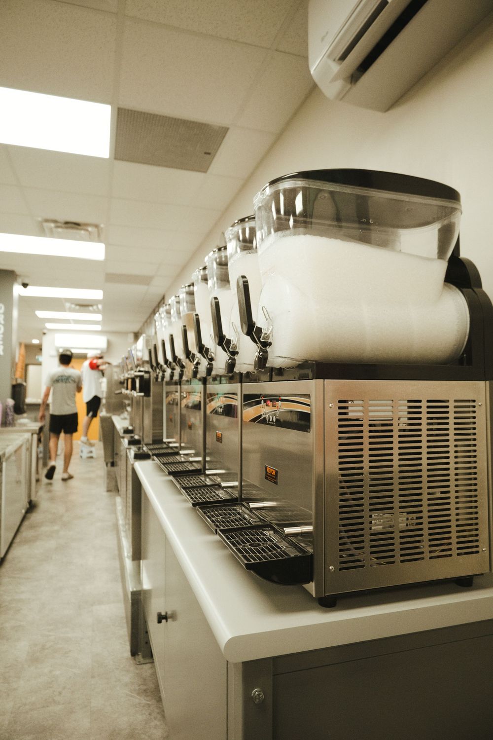 Row of commercial slushie machines lined up on a counter in a food service establishment.