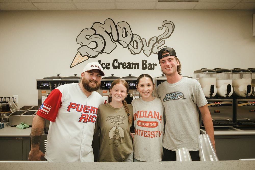 Four friends smile together at Snoov Ice Cream Bar, wearing casual shirts including Puerto Rico and Indiana University tees.