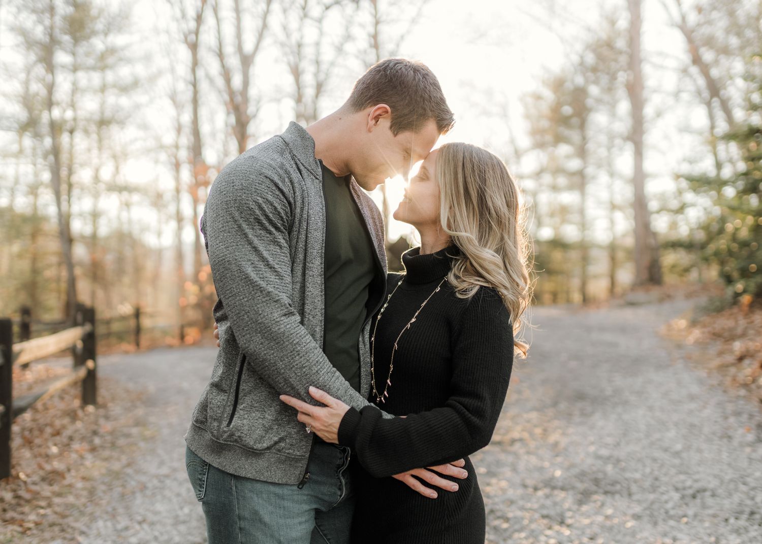 Romantic couple sharing an intimate moment on a scenic path surrounded by autumn trees during an outdoor engagement photo session.
