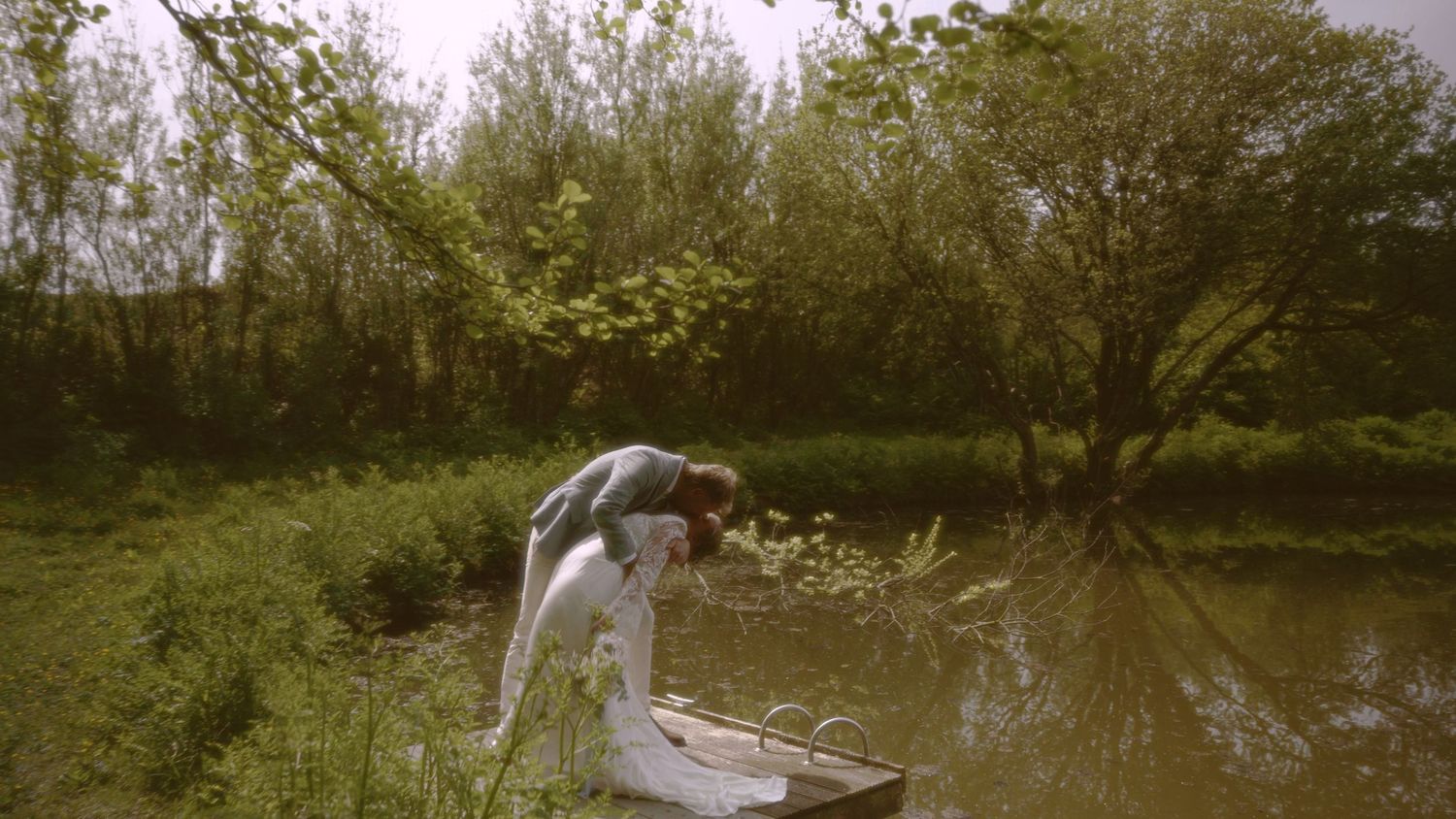 Person bending over a small boat by a tranquil pond surrounded by lush green trees and vegetation.