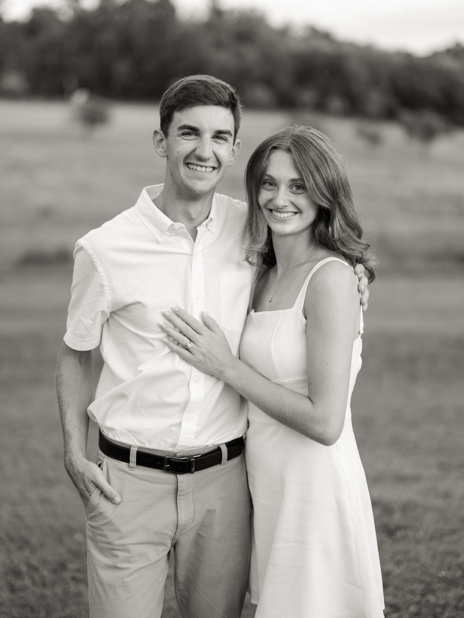 Black and white portrait of a smiling engaged couple in an open field.