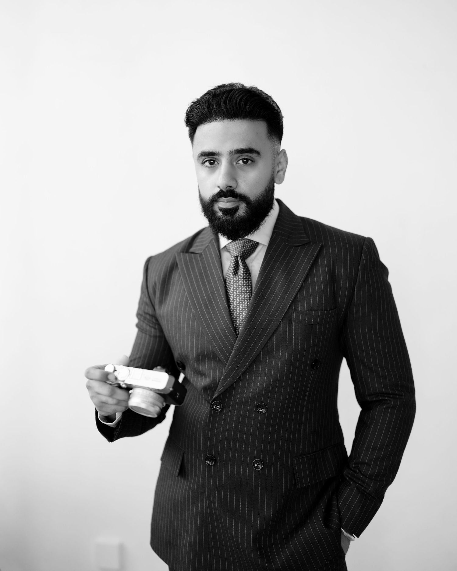 A professional man in a dark pinstripe suit holding a book, posing confidently in a well-lit modern interior.