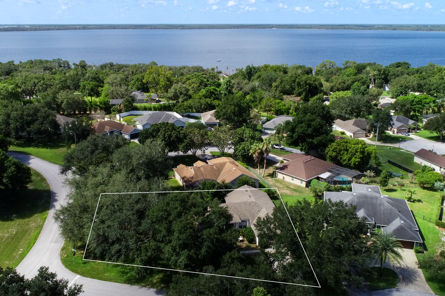 Aerial view of a residential lot outlined in white near a Florida waterfront, surrounded by lush trees and neighboring homes.