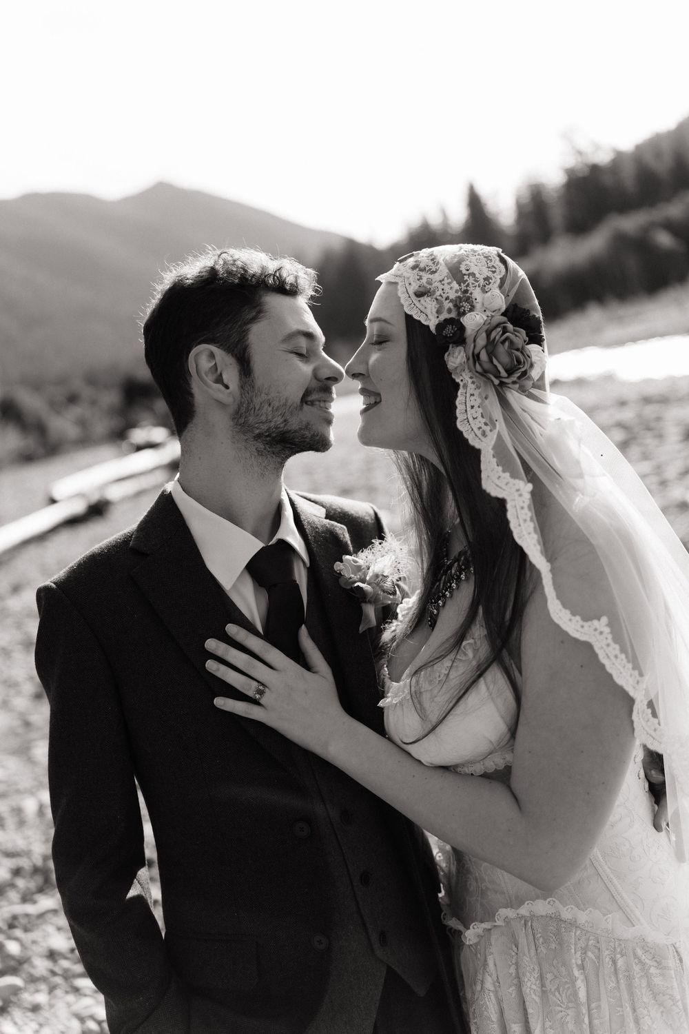 Black and white portrait of a smiling bride and groom embracing outdoors with mountains visible behind them.