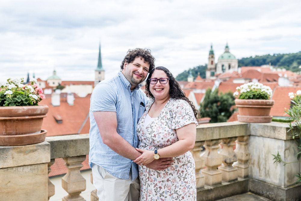 Couple embracing on a terrace with Prague red rooftops and church spires in the background.