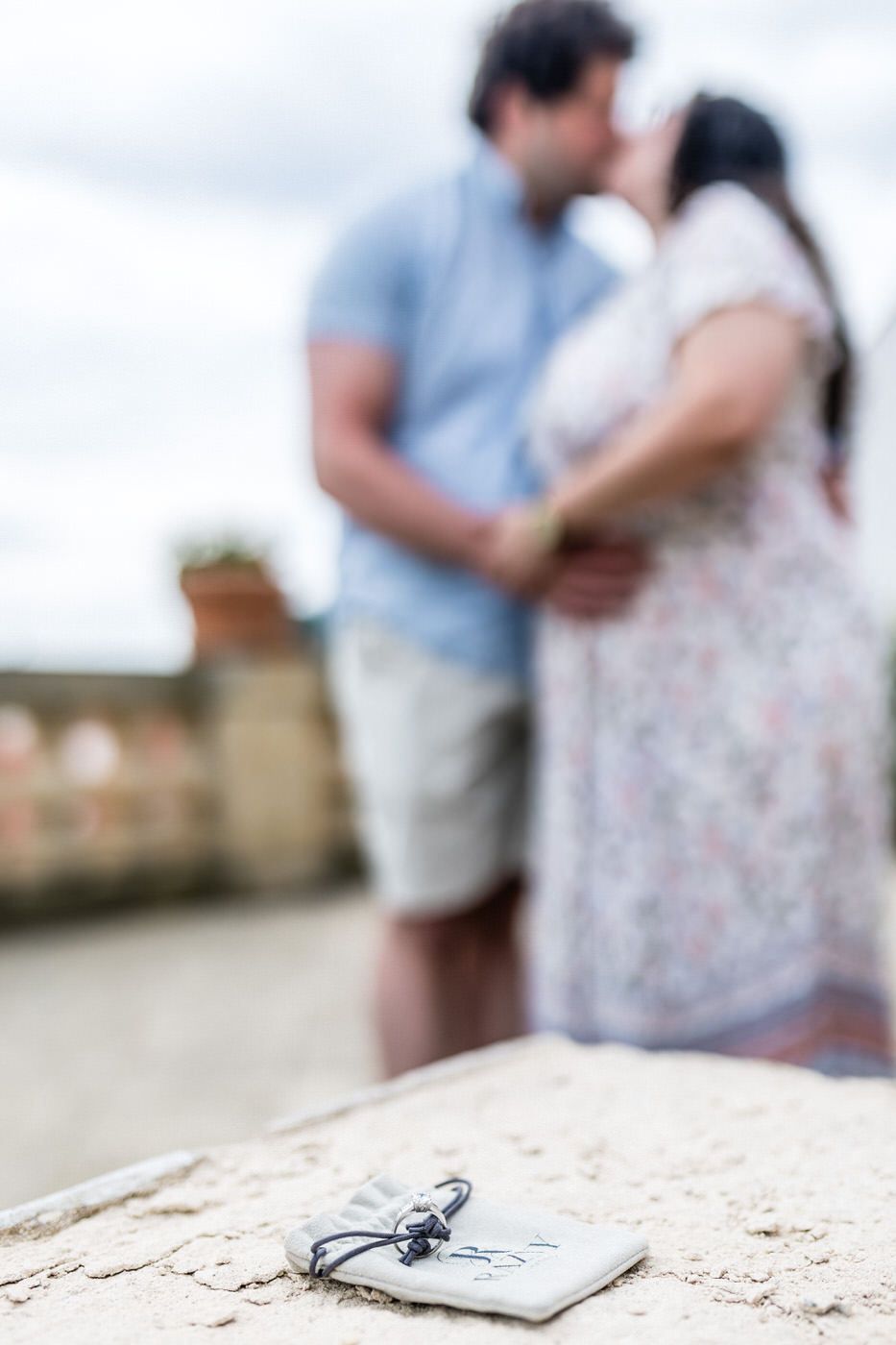 Couple kissing on rooftop with keys and notepad in foreground, romantic engagement moment outdoors.