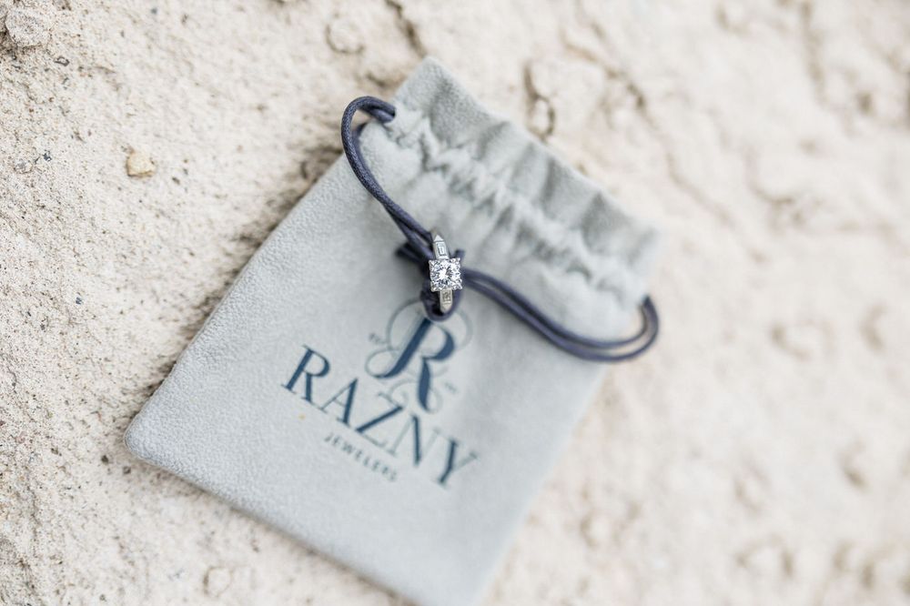 Razny Jewelers gray velvet pouch with a diamond ring bracelet displayed on sandy beach background.