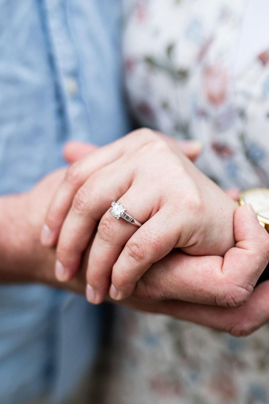 Close-up of an engagement ring with a diamond solitaire on a woman's hand held by her partner.