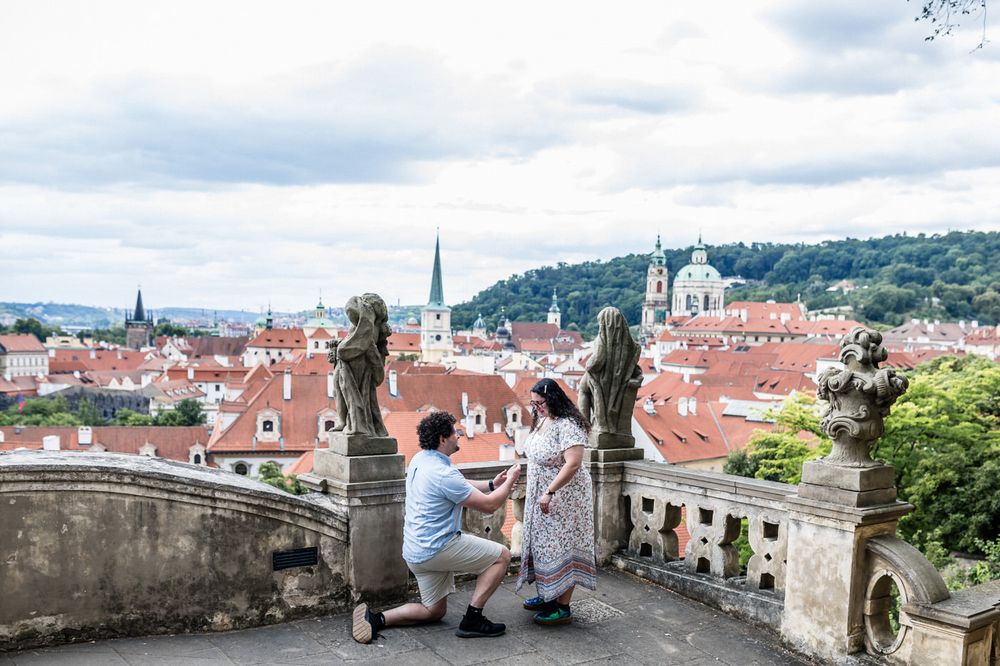 Romantic marriage proposal on a terrace overlooking Prague's red rooftops and historic skyline.