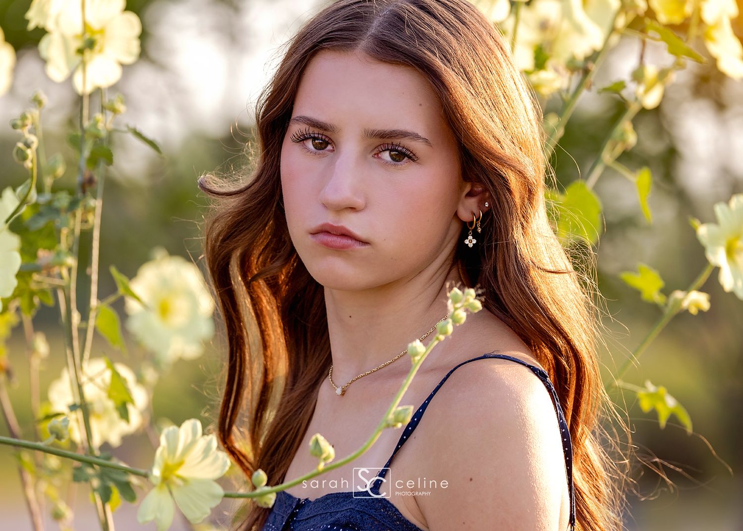 Teen girl with auburn hair poses among yellow flowers in a soft-focus outdoor portrait session.