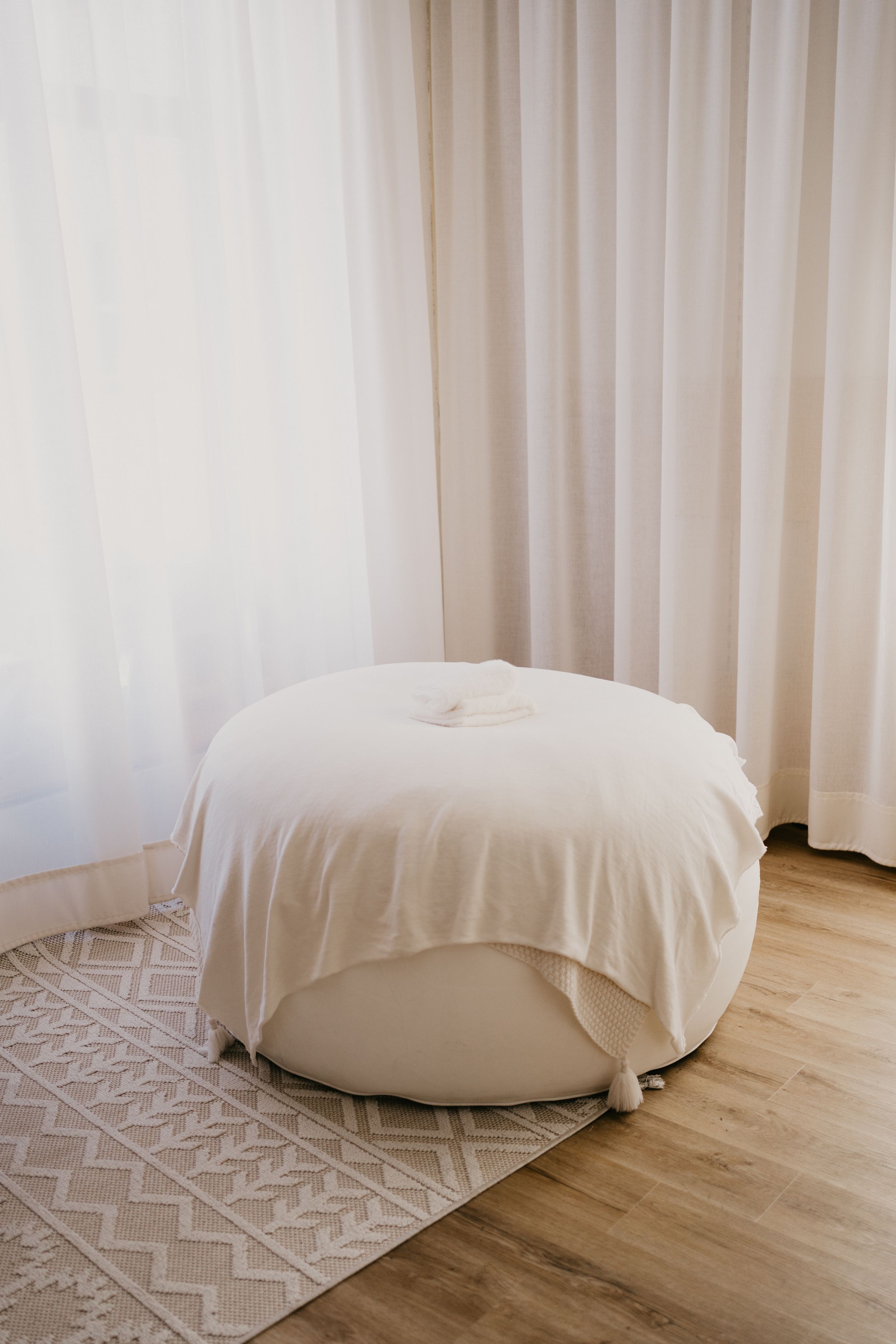 A series of five photos showing a round white bean bag chair on hardwood flooring with a geometric patterned rug.