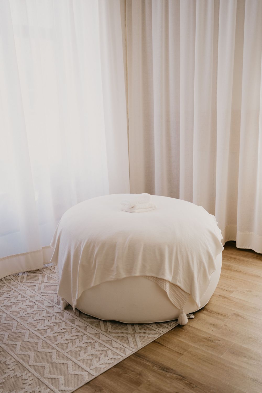 A series of five photos showing a round white bean bag chair on hardwood flooring with a geometric patterned rug.