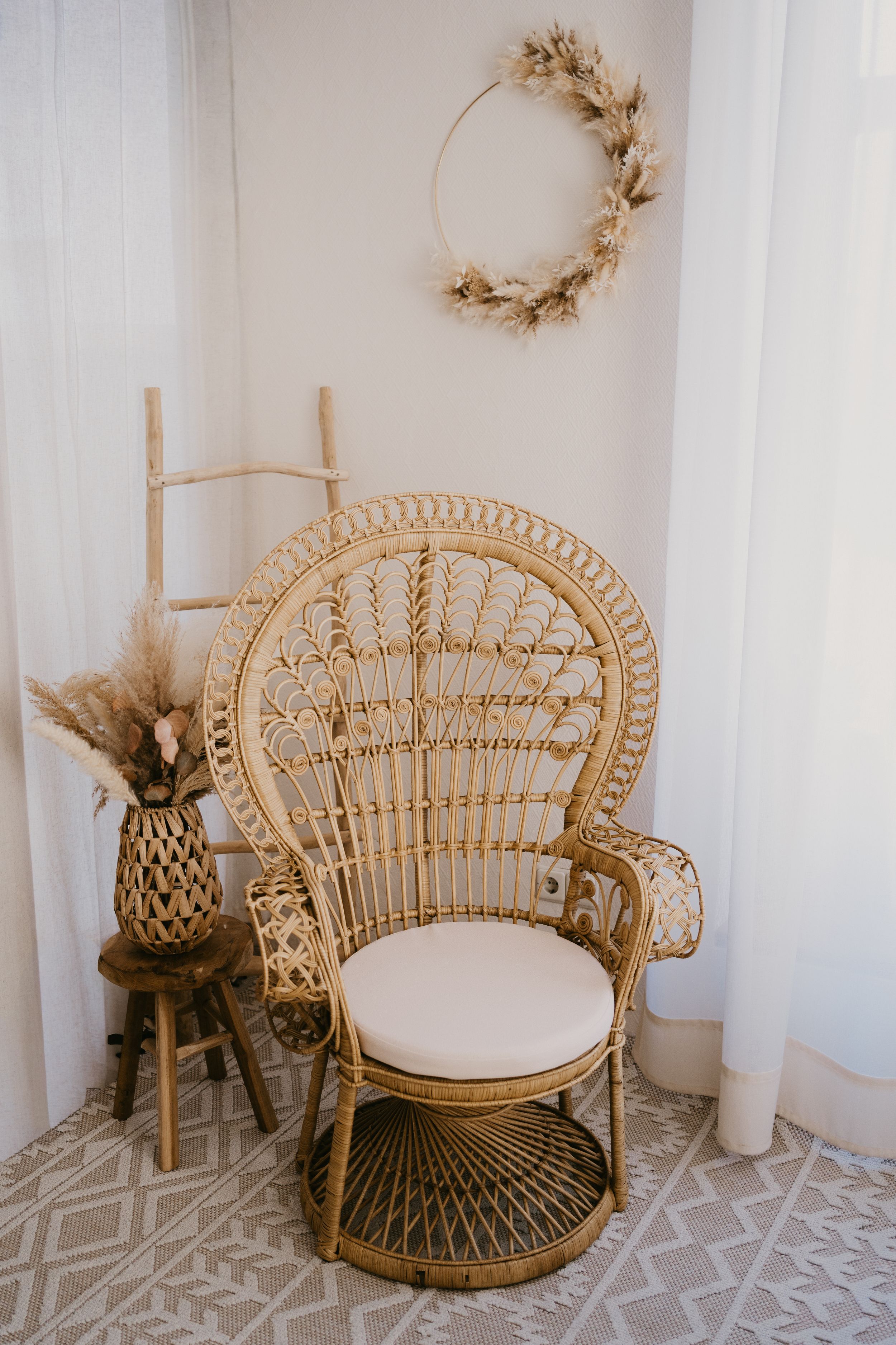 Three boho rattan peacock chairs with white cushions sit against a white wall with dried floral wreaths and decorations.