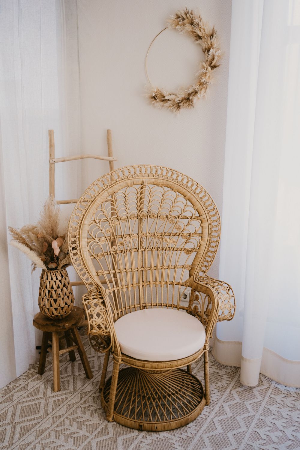 Three boho rattan peacock chairs with white cushions sit against a white wall with dried floral wreaths and decorations.
