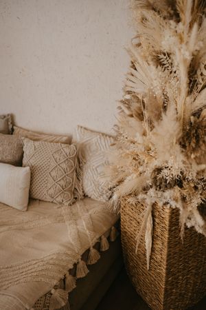 Cozy boho bedroom corner with pampas grass decor, textured throw pillows and woven basket in warm sepia tones.