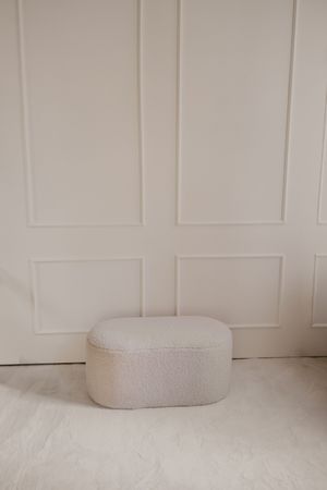 White minimalist interior wall with paneling and a round beige cushion on a light-colored surface.