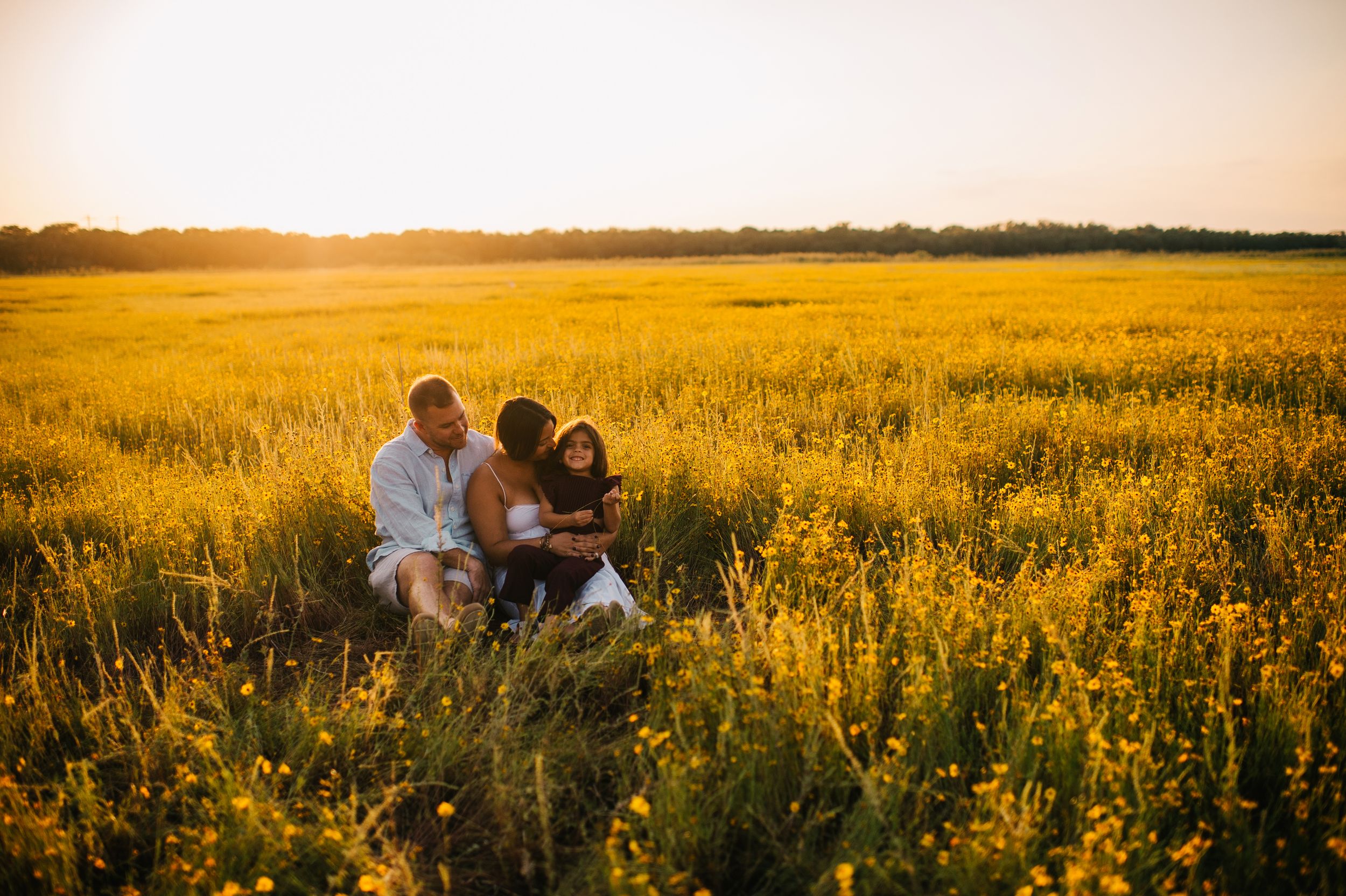 Family sitting together in golden sunflower field at sunset, bathed in warm light.