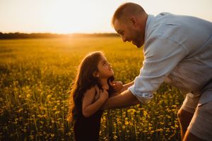 A father and daughter share a tender moment in a golden sunlit flower field at sunset.