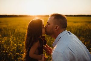 Father and daughter share a tender kiss at golden hour in a sunlit flower field.