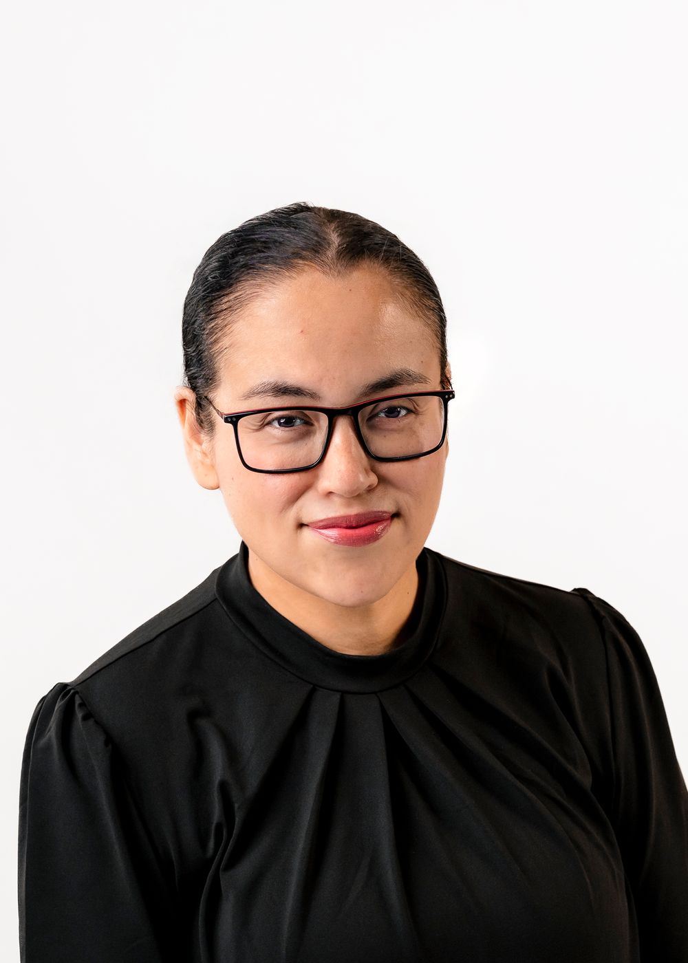 Professional headshot of a woman with glasses and dark hair, wearing a black blouse, smiling against white background.