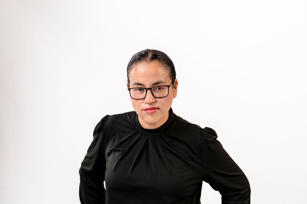 Professional woman in black top and glasses posing confidently against a white background.