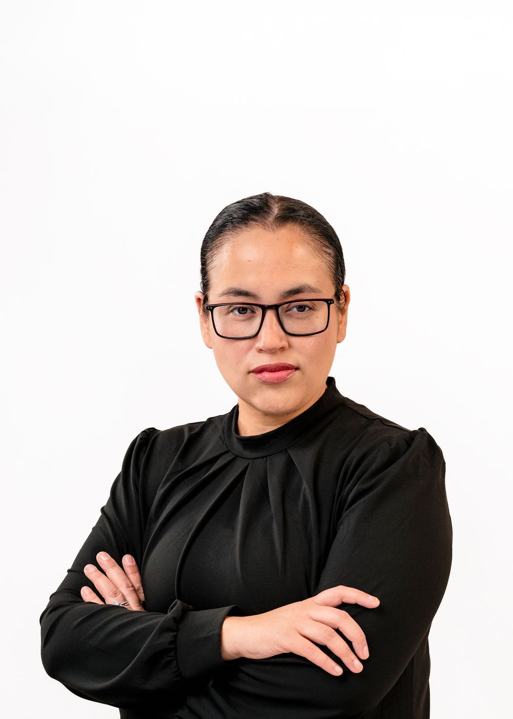 Professional woman in black top and glasses with arms crossed against white background.