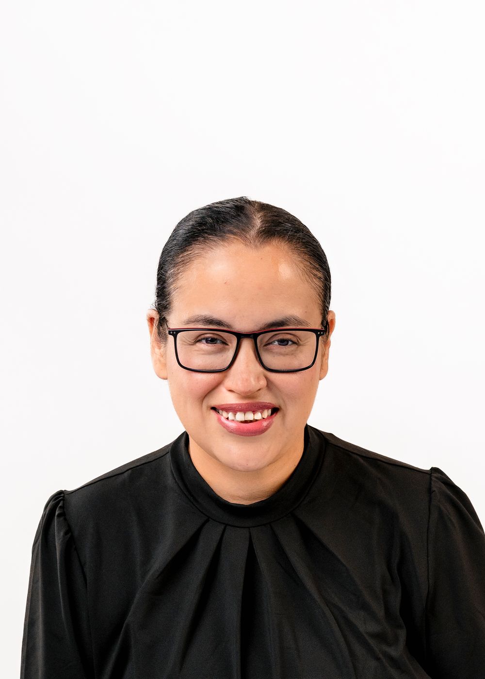 Smiling woman with glasses and dark hair wearing a black top, professional headshot on white background.