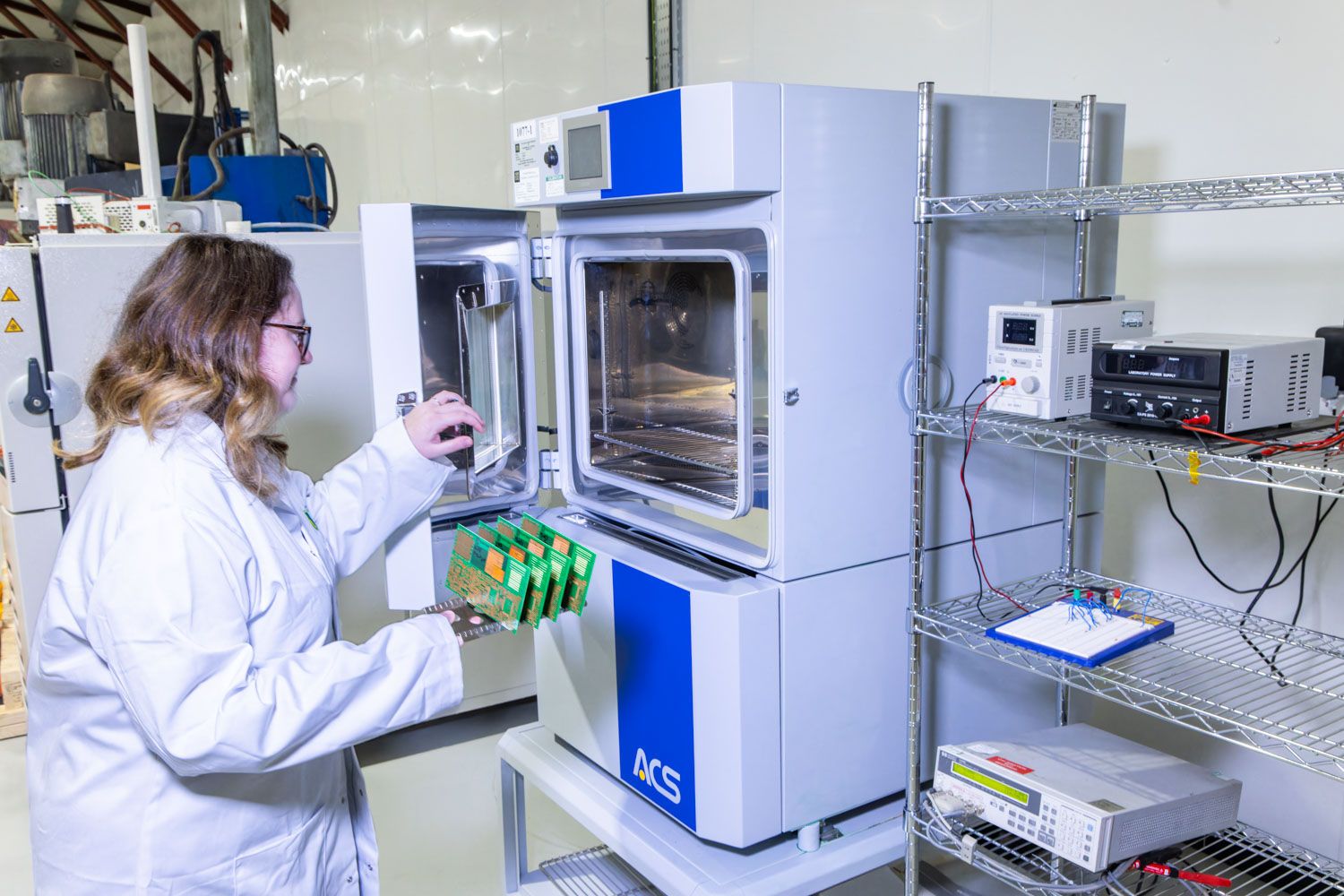 Female scientist in white lab coat operating a blue IKA laboratory oven in a modern research lab.