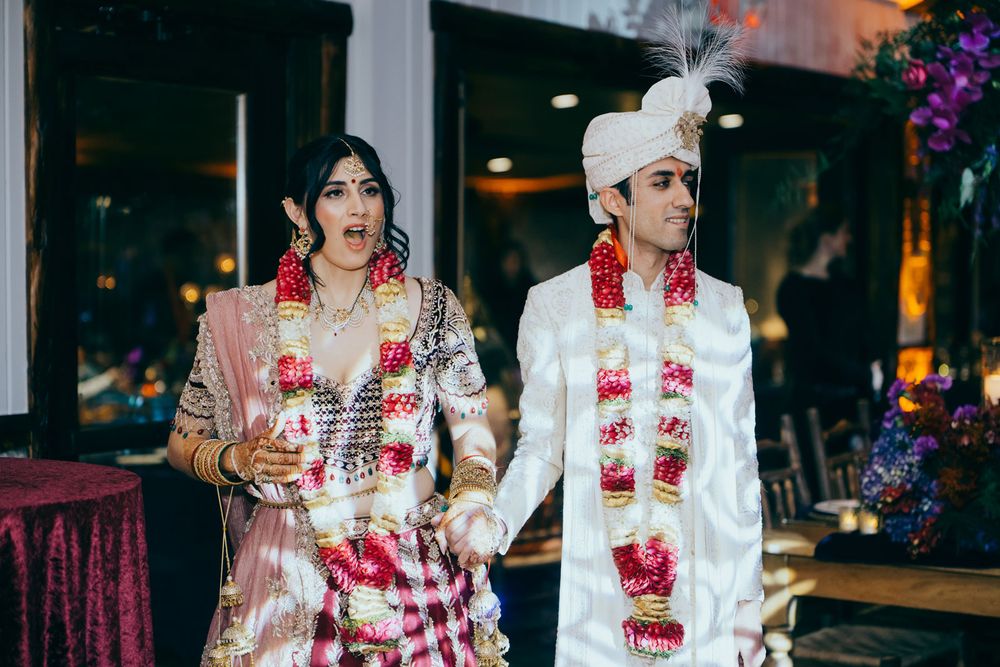 Indian bride and groom in traditional wedding attire with floral garlands walking together at a vibrant ceremony.
