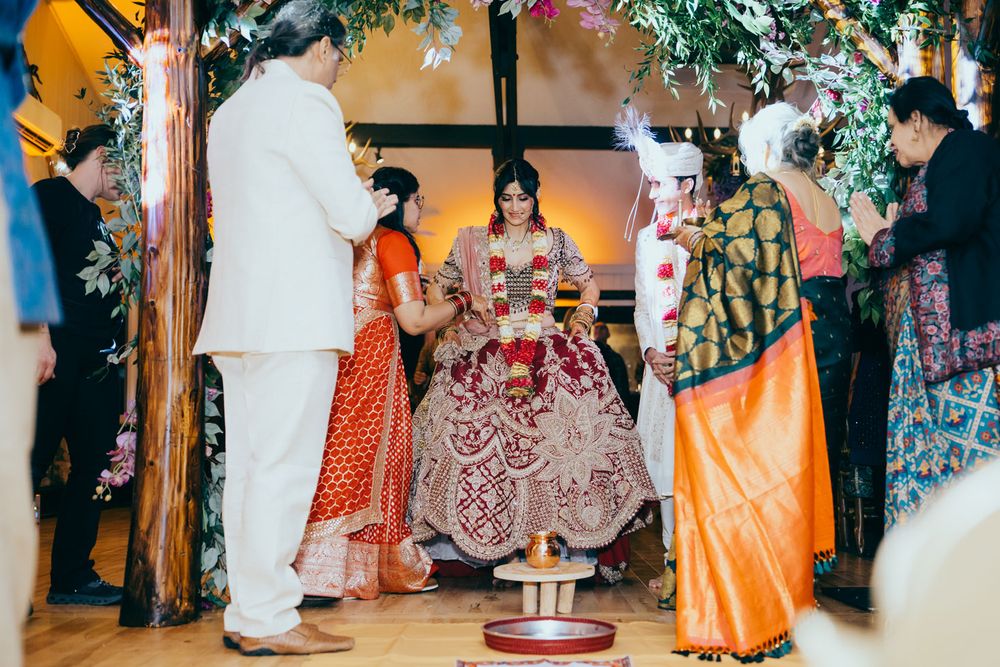 Bride in ornate red and gold lehenga during traditional Indian wedding ceremony under floral mandap with guests.