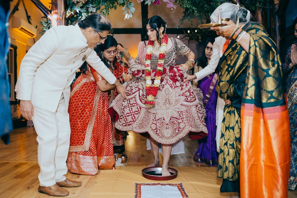 Indian wedding ceremony with bride in red lehenga being lifted during traditional ritual, surrounded by family in colorful attire.