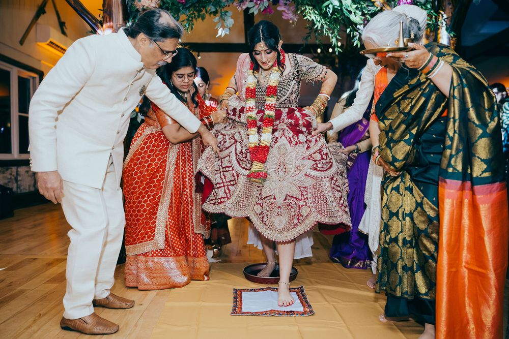 Bride in traditional Indian wedding attire steps on ritual mat surrounded by family during Hindu ceremony.