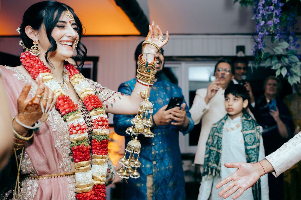 A bride in traditional South Asian attire dances joyfully wearing floral garlands and ornate jewelry at a wedding celebration.
