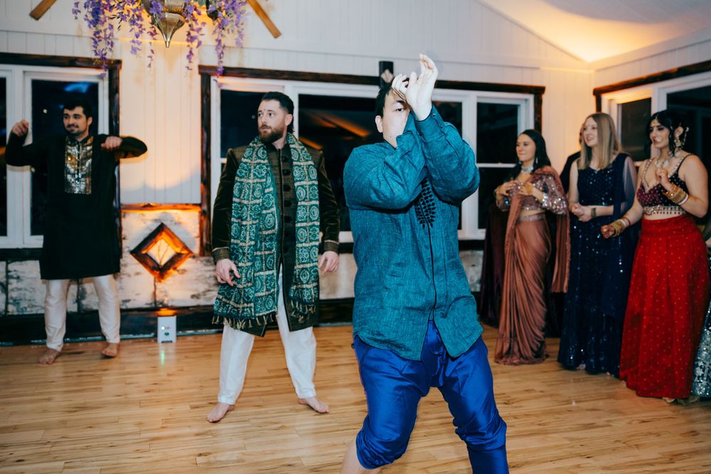 Men in traditional Indian attire dancing at a wedding reception celebration with guests watching in background.